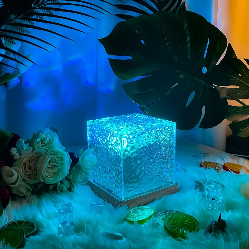 Decorative crystal cube with glowing blue light on a soft surface with flowers and leaves.